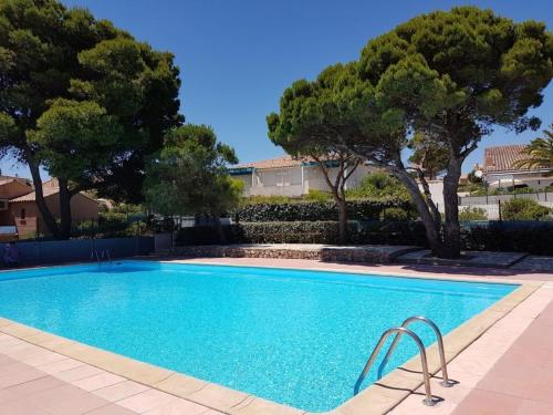 une piscine avec des arbres en arrière-plan dans l'établissement Villa T3 Mezzanine avec Piscine, Terrasse et Parking Privé, 5 min de la Plage - Narbonne - FR-1-409-37, à Narbonne-Plage
