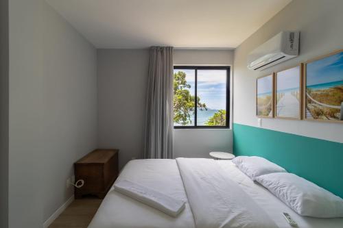 ein Schlafzimmer mit einem weißen Bett und einem Fenster in der Unterkunft Sossego frente mar com vista para a ilha CCA201 in Florianópolis