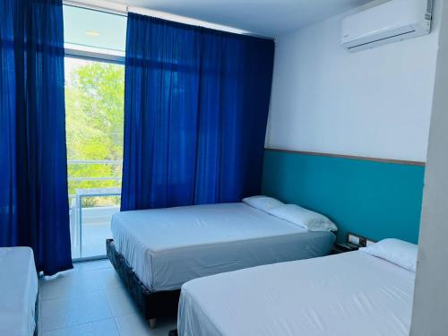 2 camas en una habitación con cortinas azules y ventana en Finca en Ricaurte La Puerta del Ángel, en Ricaurte