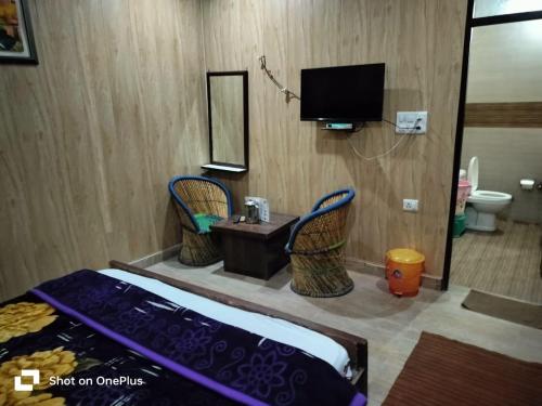 a bedroom with a bed and two chairs and a tv at Silver Dew Resorts and Restaurant in Dhanaulti