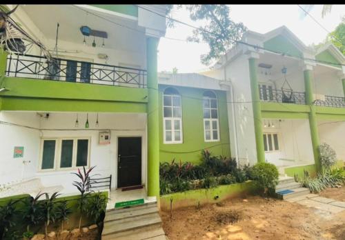 ein großes weißes und grünes Haus mit einer Veranda in der Unterkunft Goa Suites Holiday Home in Calangute