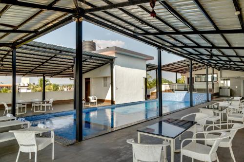 a swimming pool with white chairs and tables on a patio at La baga Beach Hotel in Calangute