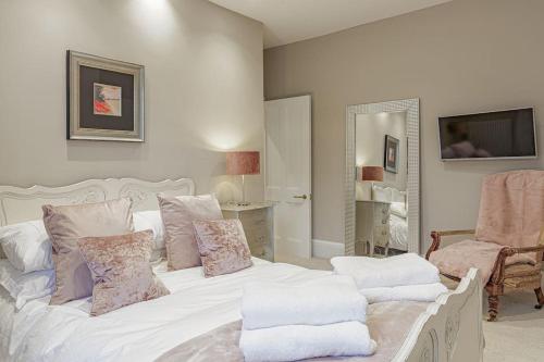 a bedroom with a white bed with pillows and a chair at Clarence House: 4BD Georgian Townhouse in Cheltenham