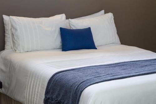 Una cama blanca con una almohada azul. en Waterford Executive Apartments en Mbabane