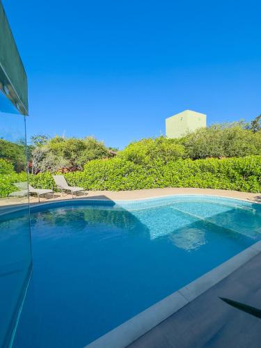 a blue swimming pool with chairs and trees at Rancho Litoral Búzios in Búzios