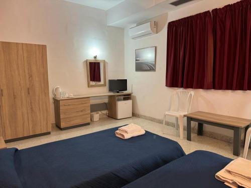 a room with two beds and a desk with a television at Roma Hotel in Sliema