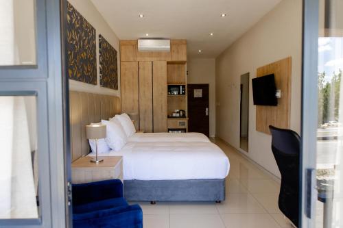 a bedroom with a white bed and a blue chair at Acres Inn Klerksdorp in Klerksdorp