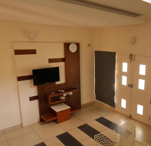a living room with a television and a clock on the wall at Royad Calicut Farm House - Premium Villa with Pool Inside a Farm in Kozhikode