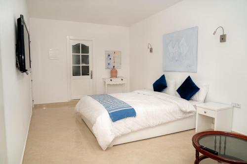 Chez Reda في أصيلة: غرفة نوم بيضاء مع سرير ووسائد زرقاء