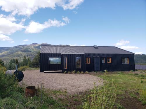 a black house in a field with mountains in the background at Casa Amapola in San Martín de los Andes