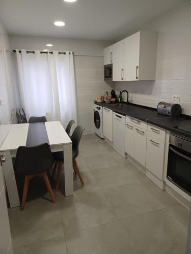 cocina con armarios blancos, mesa y sillas en Piso nuevo a 10 minutos de San Sebastián, en Lasarte