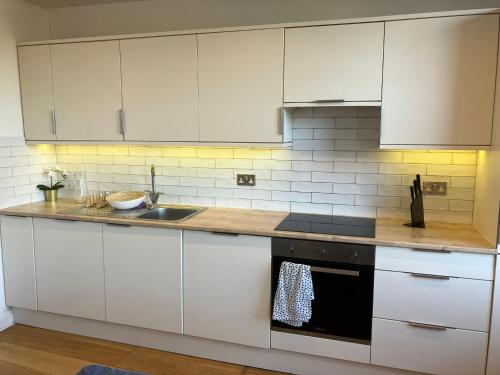 uma cozinha com armários brancos e um lavatório em Awesome Refurbished 1 Bed Flat few steps to High St ! - 2 East House em Epsom