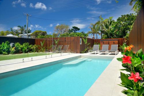 a swimming pool in a backyard with chairs and flowers at Massinger Views in Byron Bay