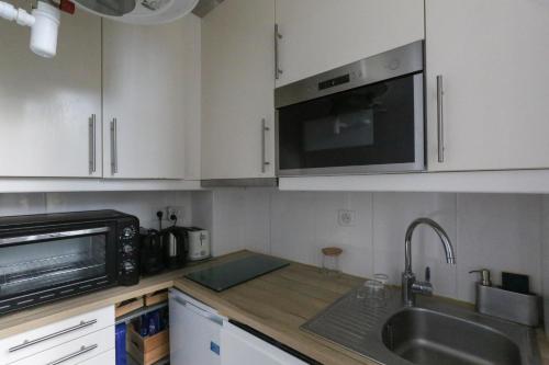 een keuken met witte kasten, een wastafel en een magnetron bij Comfortable and well-appointed 30 m apartment in Vanves