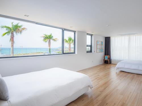 a white bedroom with palm trees and a large window at Boutique Pool Villa NAMIB in Jeju