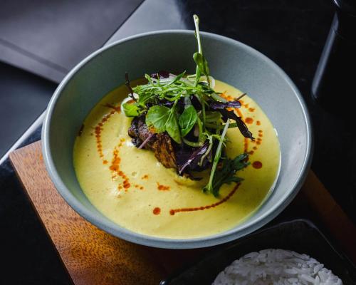 a bowl of soup with greens and rice on a table at Hotel Verge Launceston in Launceston