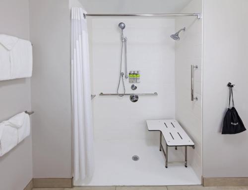 a white bathroom with a shower and a bench at Holiday Inn Express & Suites Tulsa South - Woodland Hills, an IHG Hotel in Tulsa