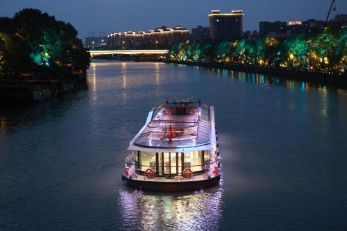 Cheery Canal Hotel Hangzhou - Intangible Cultural Heritage Hotel في هانغتشو: قارب يسافر في نهر في الليل