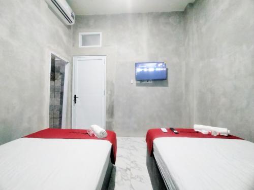 two beds in a room with a tv on a wall at RedDoorz Syariah near Exit Tol Bojong Pekalongan in Pekalongan