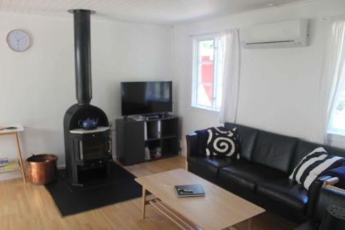 a living room with a black leather couch and a fireplace at Charming Cottage Close To The Beach in Vester Sømarken