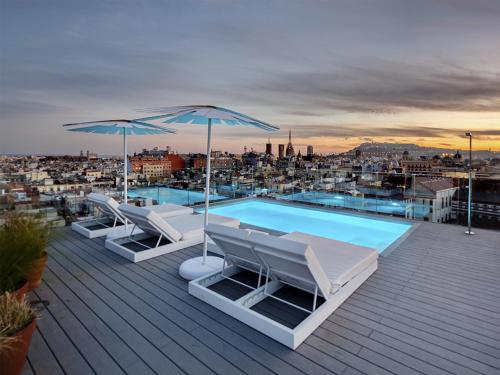 een zwembad met ligstoelen en parasols op een dak bij Yurbban Trafalgar Hotel in Barcelona