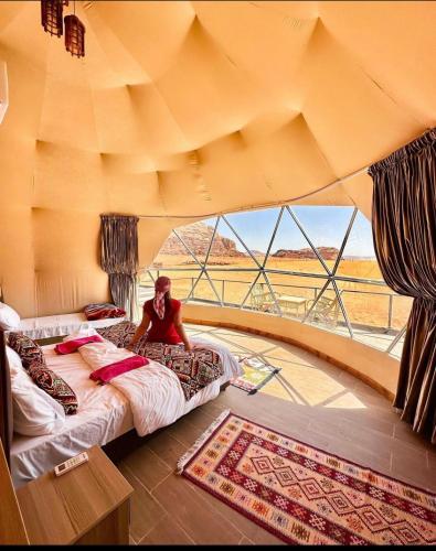 a man sitting on a bed in a room with a window at Rum Goldeneye luxury camp in Wadi Rum