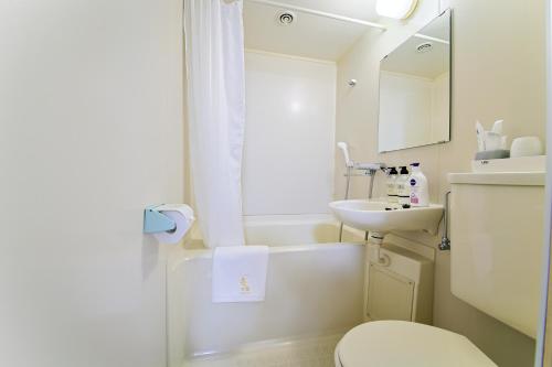 ein weißes Bad mit einem Waschbecken und einem WC in der Unterkunft ホテルよしや in Osaka