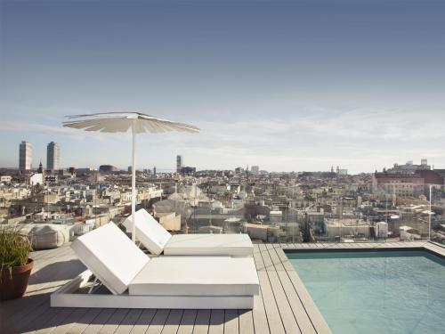 a patio with a pool and an umbrella and a chair and a swimming pool at Yurbban Trafalgar Hotel in Barcelona