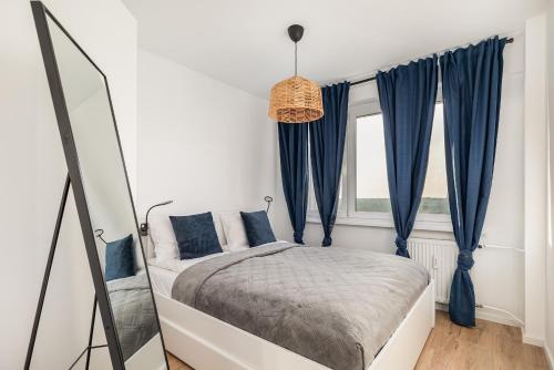 a bedroom with a bed with blue curtains and a mirror at Apartment Near the Warta River by Renters in Poznań