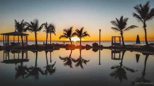 a pool of water with palm trees and a sunset at TRACADERO Beach Club & Holidays Rentals in Bayahibe