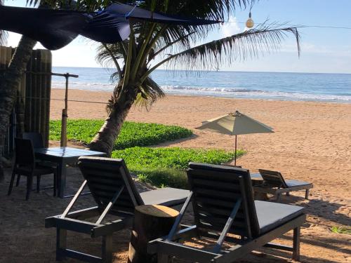 a table and chairs and an umbrella on the beach at Mandy House in Habaraduwa