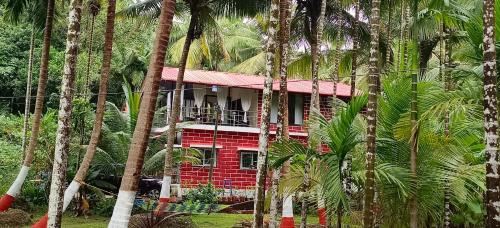 una casa roja en medio de palmeras en Walawal Bliss Farm Stay, en Vālāval
