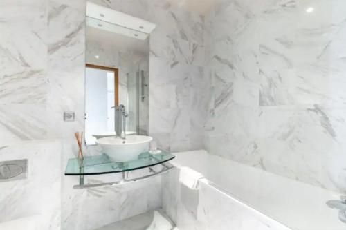 La salle de bains blanche est pourvue d'un lavabo et d'une baignoire. dans l'établissement Avenue Montaigne Luxury Apartment 2BR 4P, à Paris