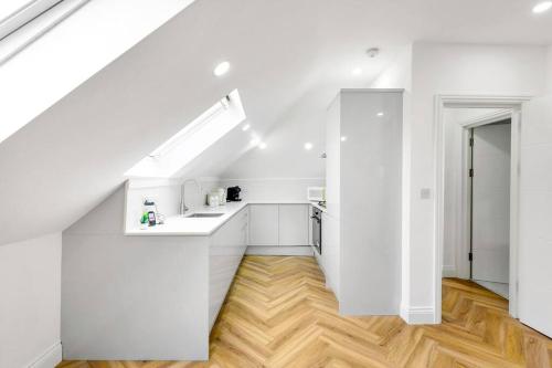 a white kitchen with white cabinets and wooden floors at Chic 4 person penthouse & views West London W7 Modern free parking (4 occupancy) in London