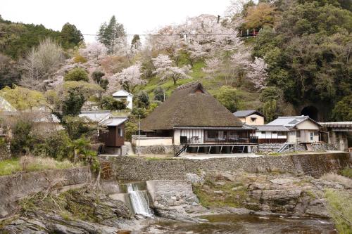 un edificio con techo de paja junto a un río en KANAU, en Gojō