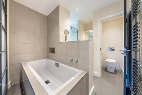 ein Badezimmer mit einer großen weißen Badewanne und einem WC in der Unterkunft Candler Mews - Twickenham in Twickenham