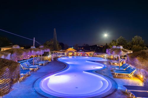 - une piscine avec des chaises bleues et la lune la nuit dans l'établissement Hotel Pedra Niedda, à Budoni