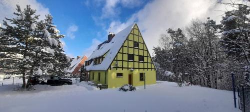 a yellow house with a christmas tree in the snow at Domek Marzeń in Mrzeżyno