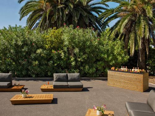 a patio with couches and tables and palm trees at ME Sitges Terramar in Sitges