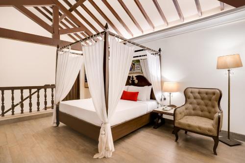 1 dormitorio con cama con dosel y silla en Lemon Tree Amarante Beach Resort, Goa, en Candolim