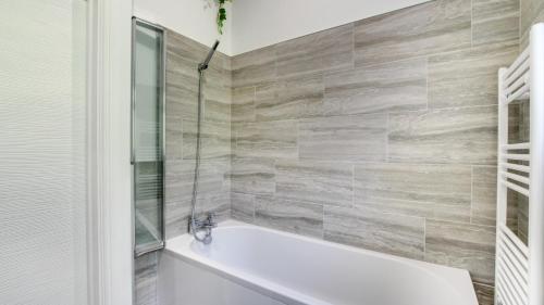 a white bath tub in a bathroom with a tile wall at Roman Bridge Close in Oystermouth