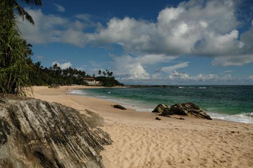 una playa de arena con rocas y el océano en MENAKA HOMESTAY en Tangalle
