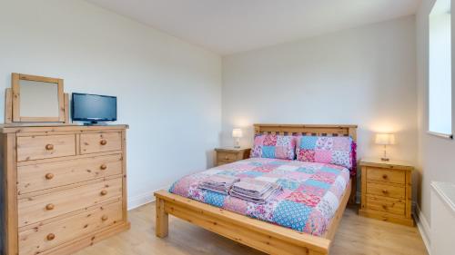 a bedroom with a bed and a dresser and a tv at Daffodil Cottage in Penclawdd