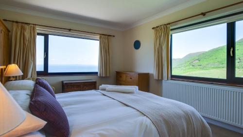 a bedroom with a bed and two large windows at Caemor in Rhossili