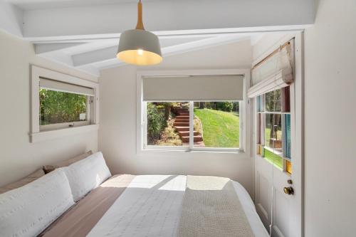 a white bedroom with a bed and two windows at Piha - City Escape, Piha Holiday Home in Piha
