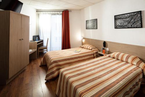 a hotel room with two beds and a desk at Hôtel Hélianthe in Lourdes