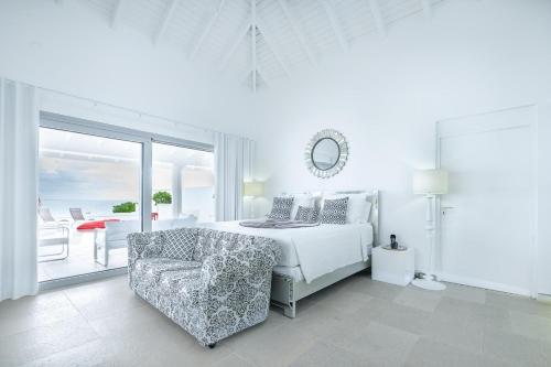 a white bedroom with a bed and a chair at La Perla Estate - 7 BR Luxury Beachfront Villa with utmost privacy in Les Terres Basses