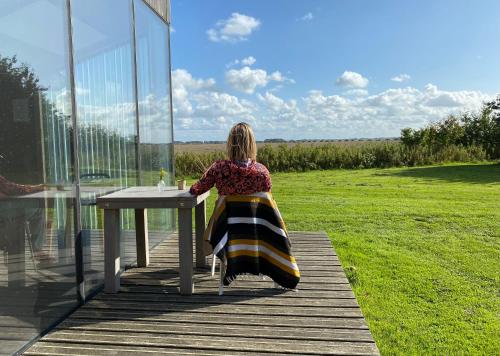 a woman sitting at a table in a glass house at Slapen aan het Wad in Rasquert