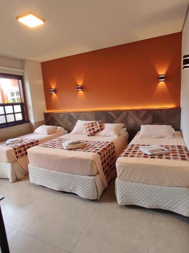 three beds in a room with orange walls at Pousada Novo Prado in Prado