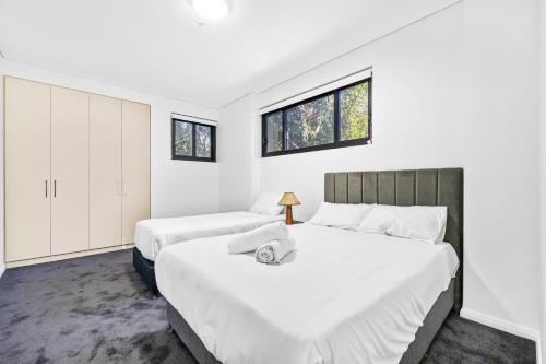 2 camas en un dormitorio con paredes y ventanas blancas en Urban Oasis in Heart of Homebush en Sídney